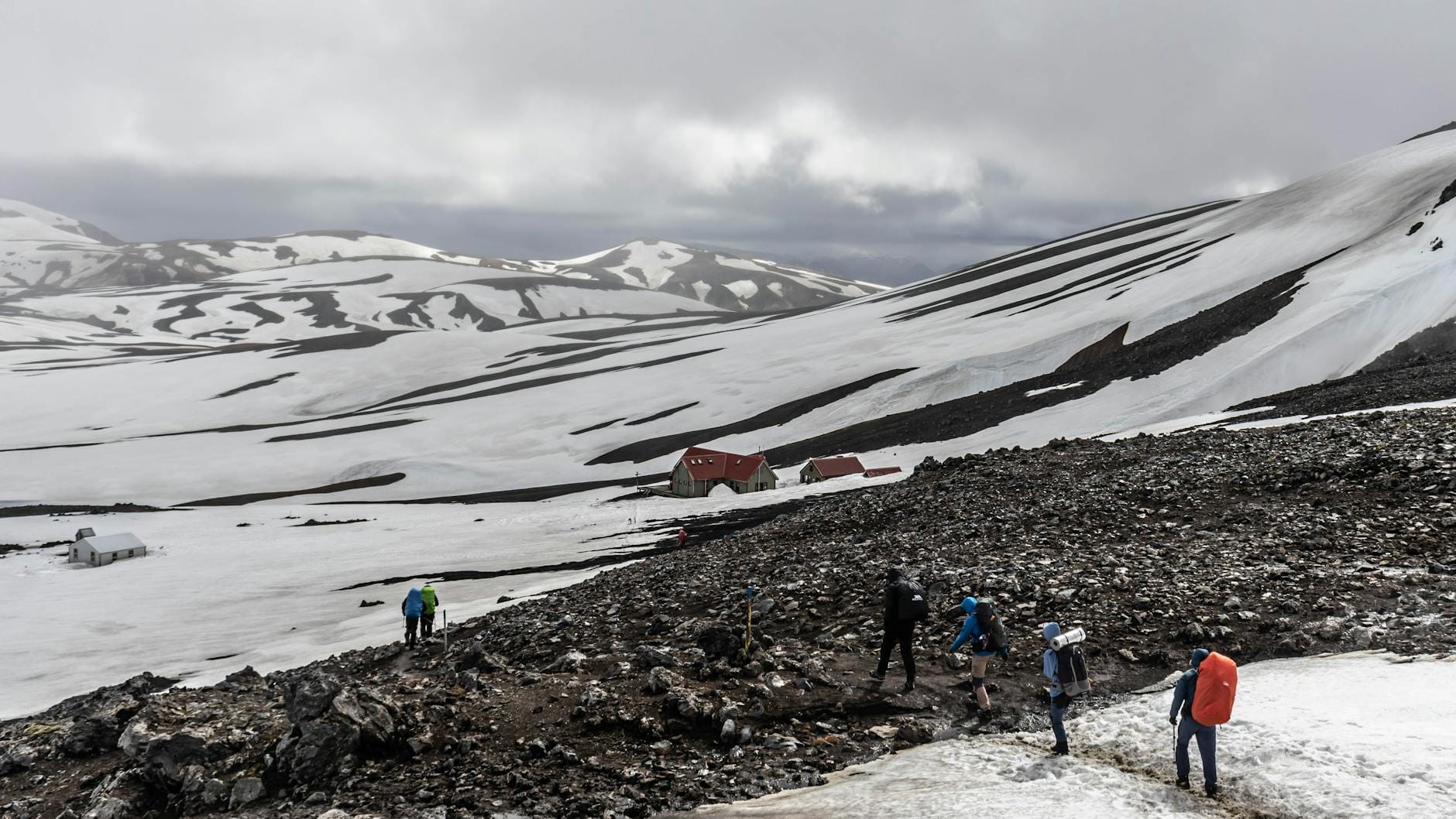 Turyści z plecakami idą po ośnieżonych zboczach w surowych górach