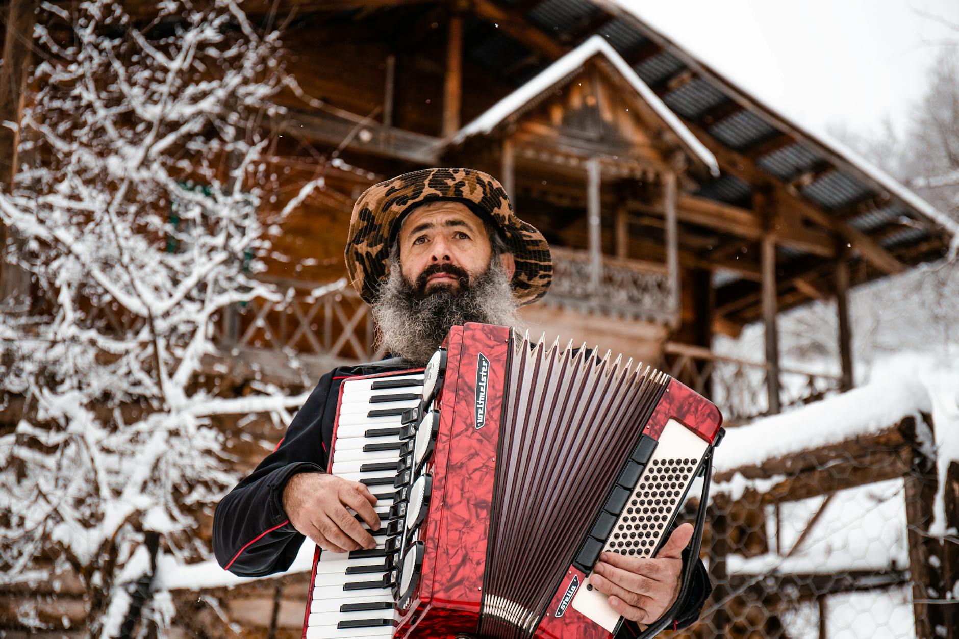 Spotkania z góralami: wieczory regionalne w Zakopanem bez kiczu Brodaty góral gra na akordeonie przed drewnianym domem w śniegu