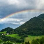 Tęcza nad zielonymi, deszczowymi wzgórzami w górskim pejzażu
