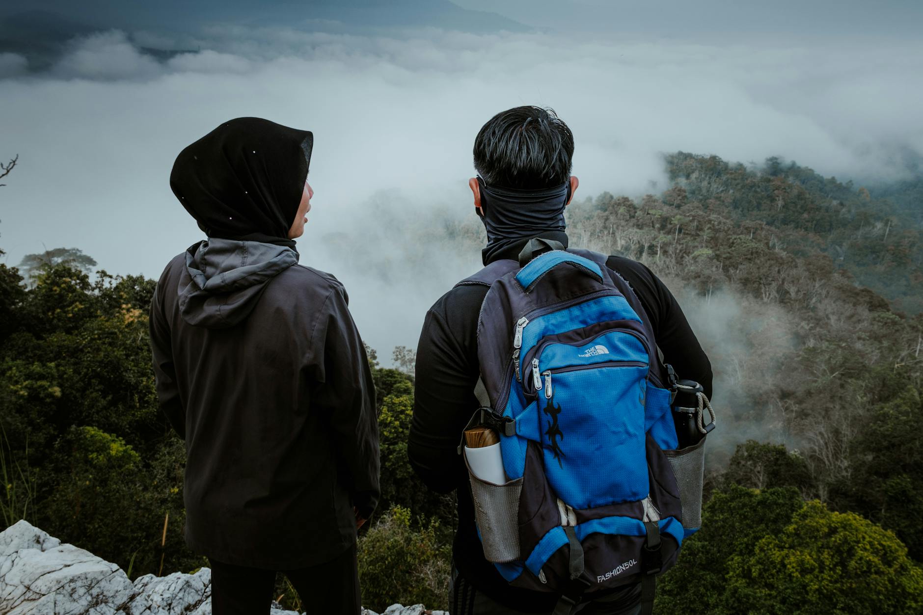 Dwóch turystów na klifie spogląda na mglisty las w malezyjskich górach