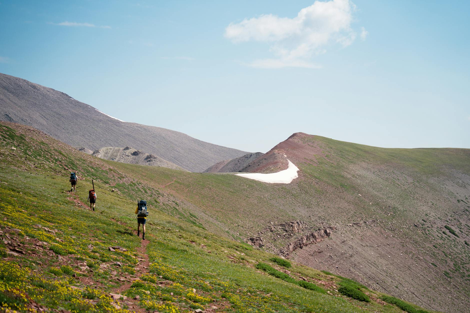 Turyści na letnim szlaku górskim pod błękitnym, lekko zachmurzonym niebem